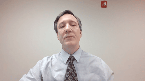 Man speaking at AIIT conference, professional setting, formal attire.