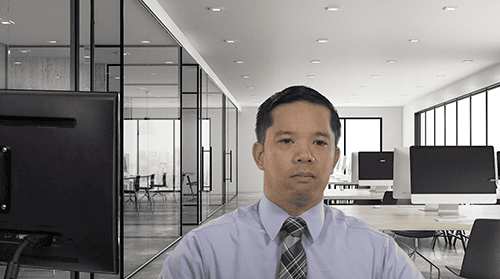 AIIT professional in a modern, bright office with glass walls and multiple computer workstations.